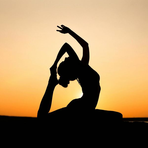 Silhouette of a person in a powerful yoga warrior pose at sunset.